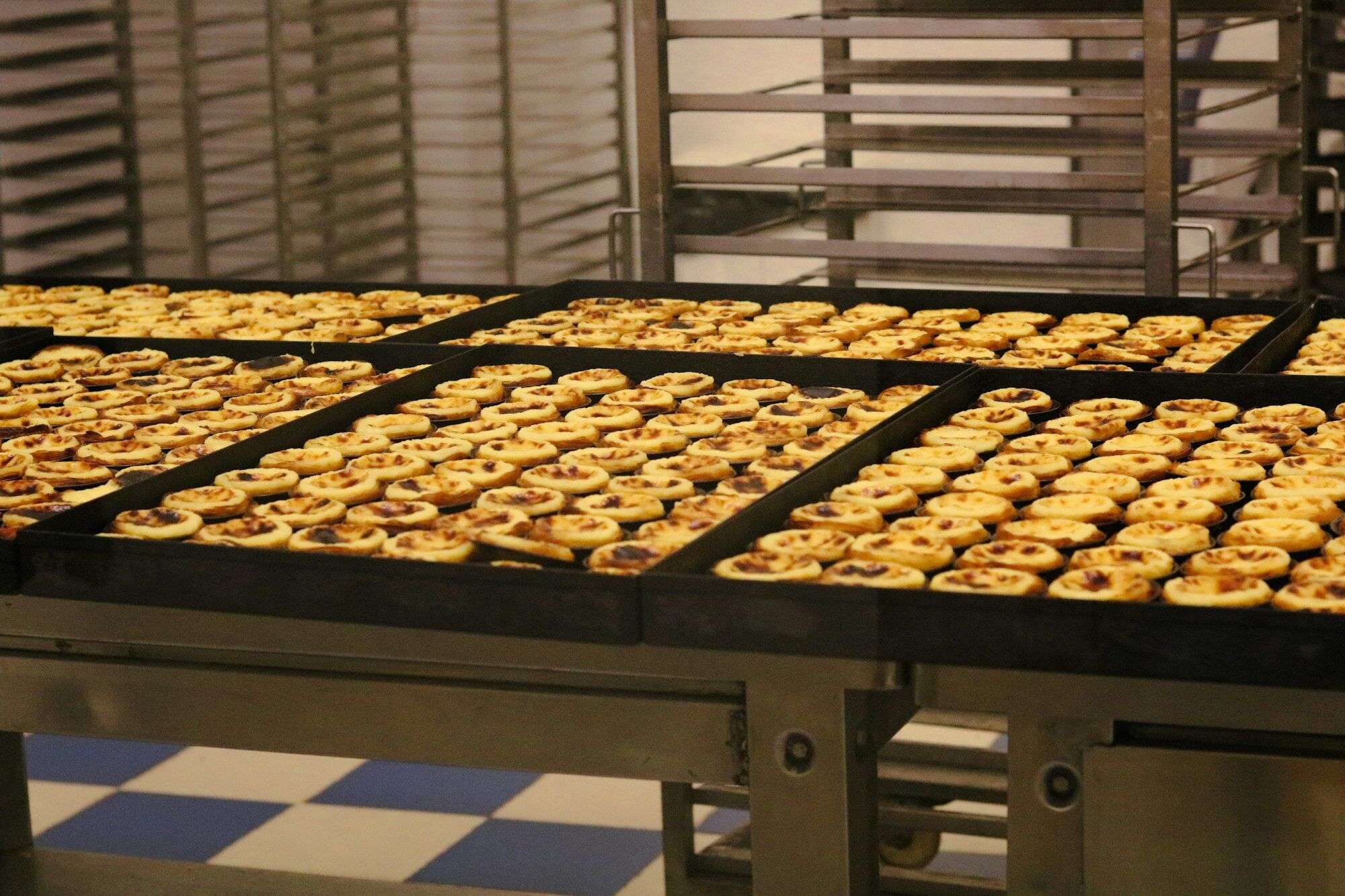 Trays of baked pastries on a bakery production line beside oven racks