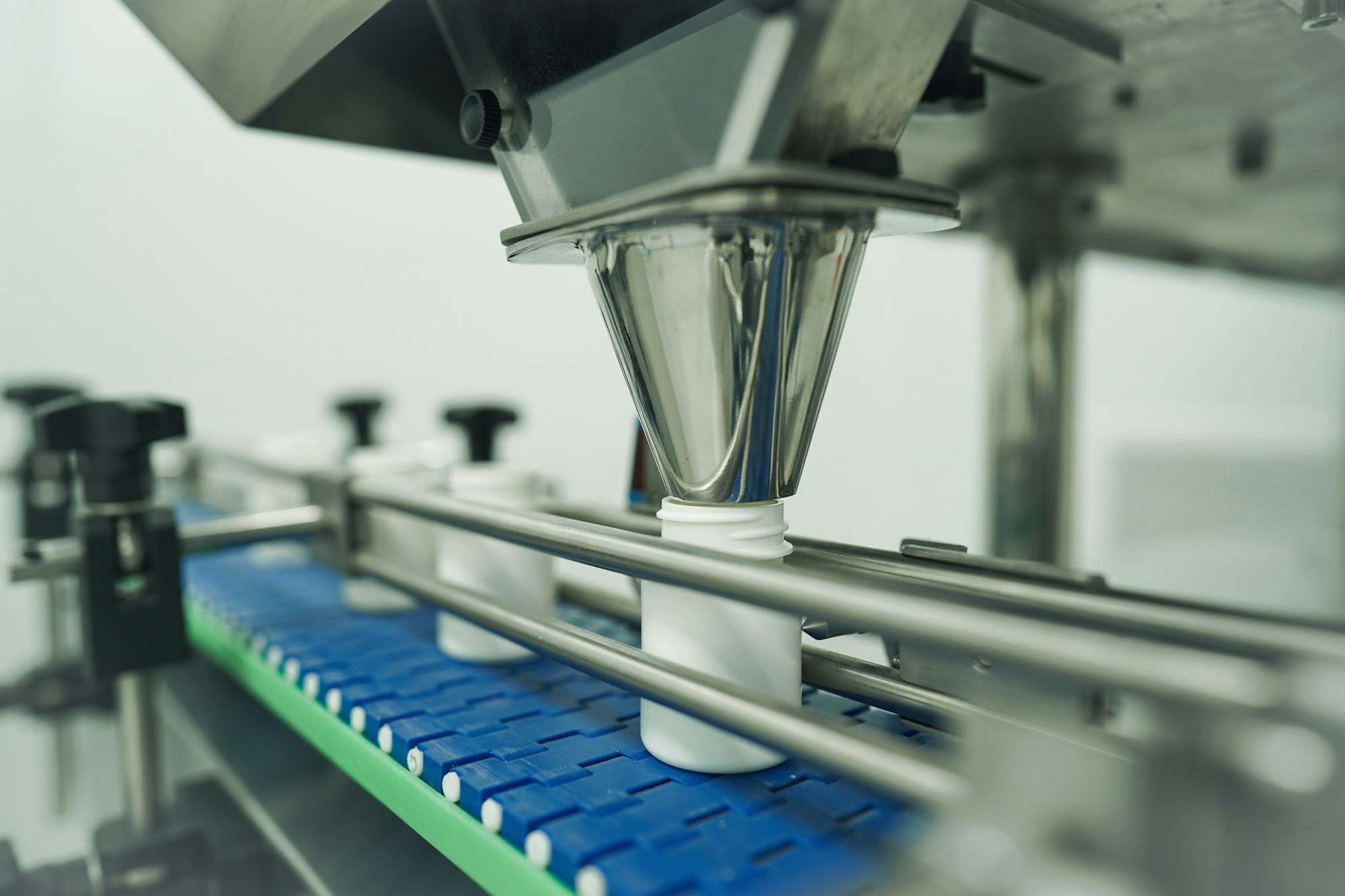 Stainless powder-filling head dispensing into white tubs on an automated conveyor line