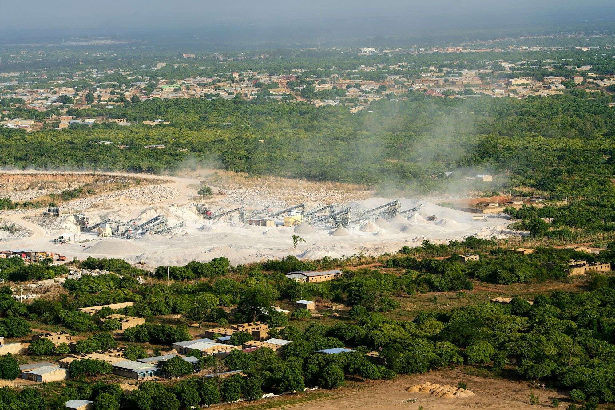 Aerial view of quarry dust rising from crushing and screening plant and stockpiles at an open quarry