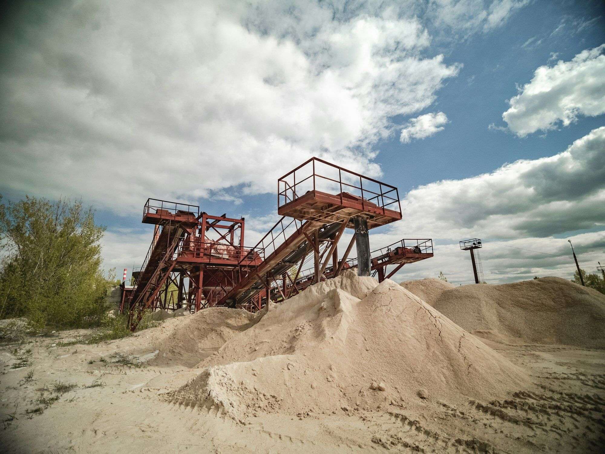Older steel crushing and screening plant with inclined conveyors above stockpiles of crushed sand