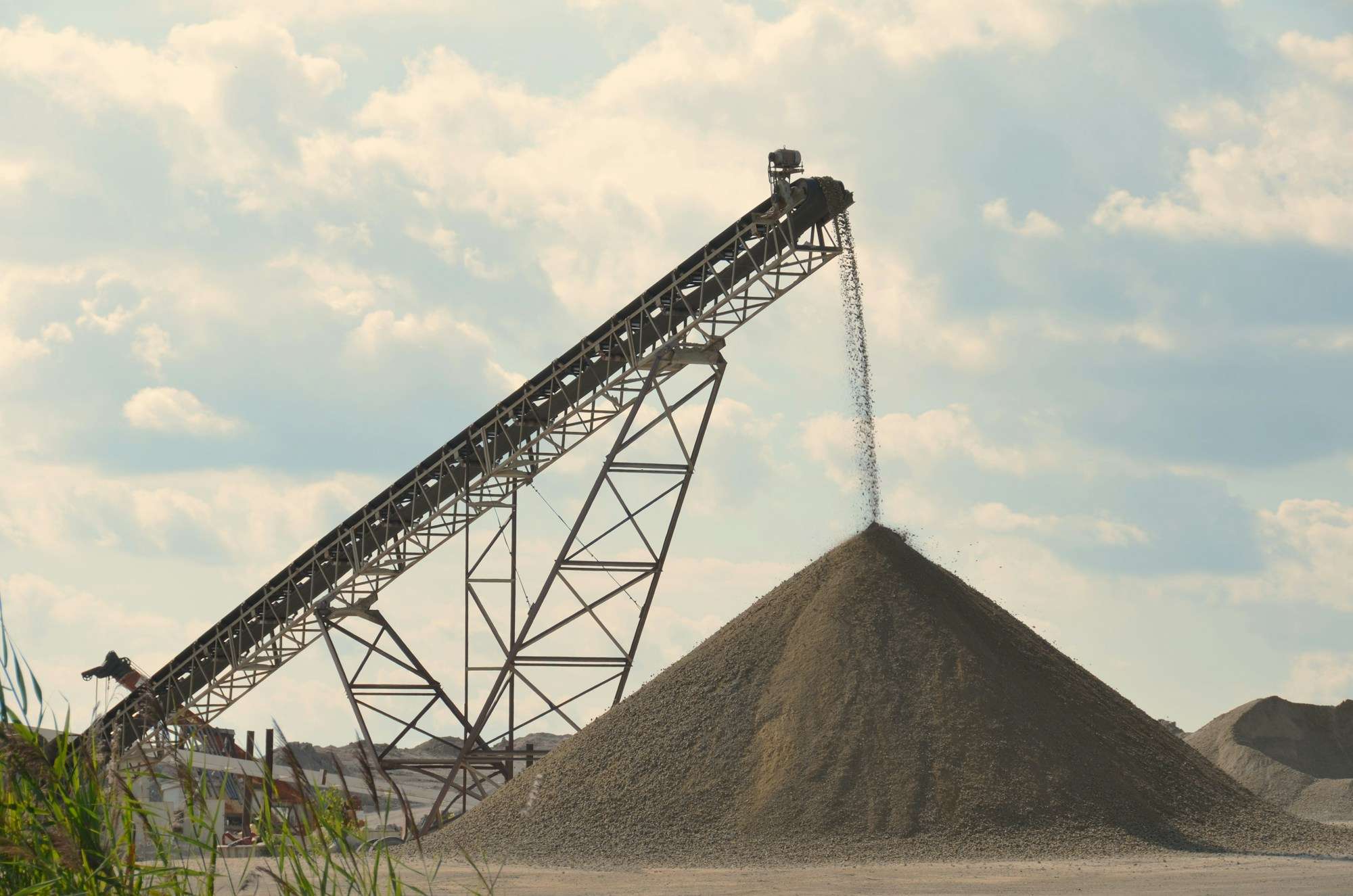 Steel conveyor at a quarry dropping crushed gravel onto a large conical stockpile
